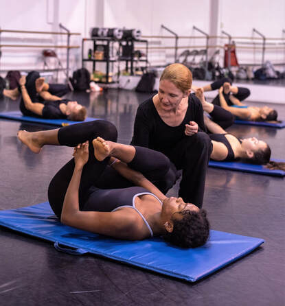 A picture of Andrea kneeling next to a student who is lying on her back stretching
